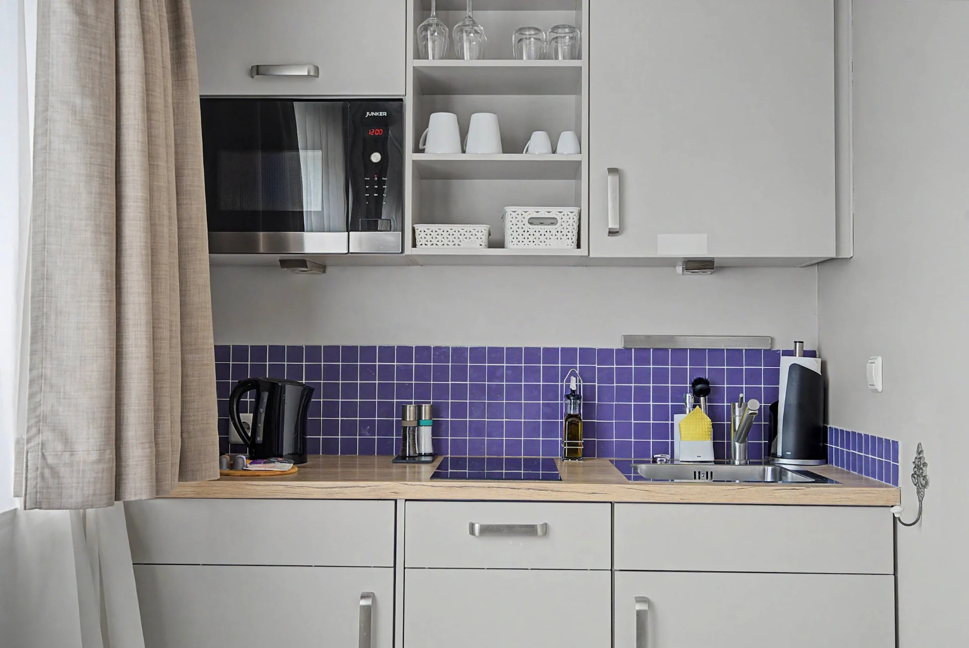 Kompakte Küchenzeile mit hellen Schränken, Holzplatte und lila Fliesenspiegel im Aparthotel-Apartment in Berlin — Innenaufnahme