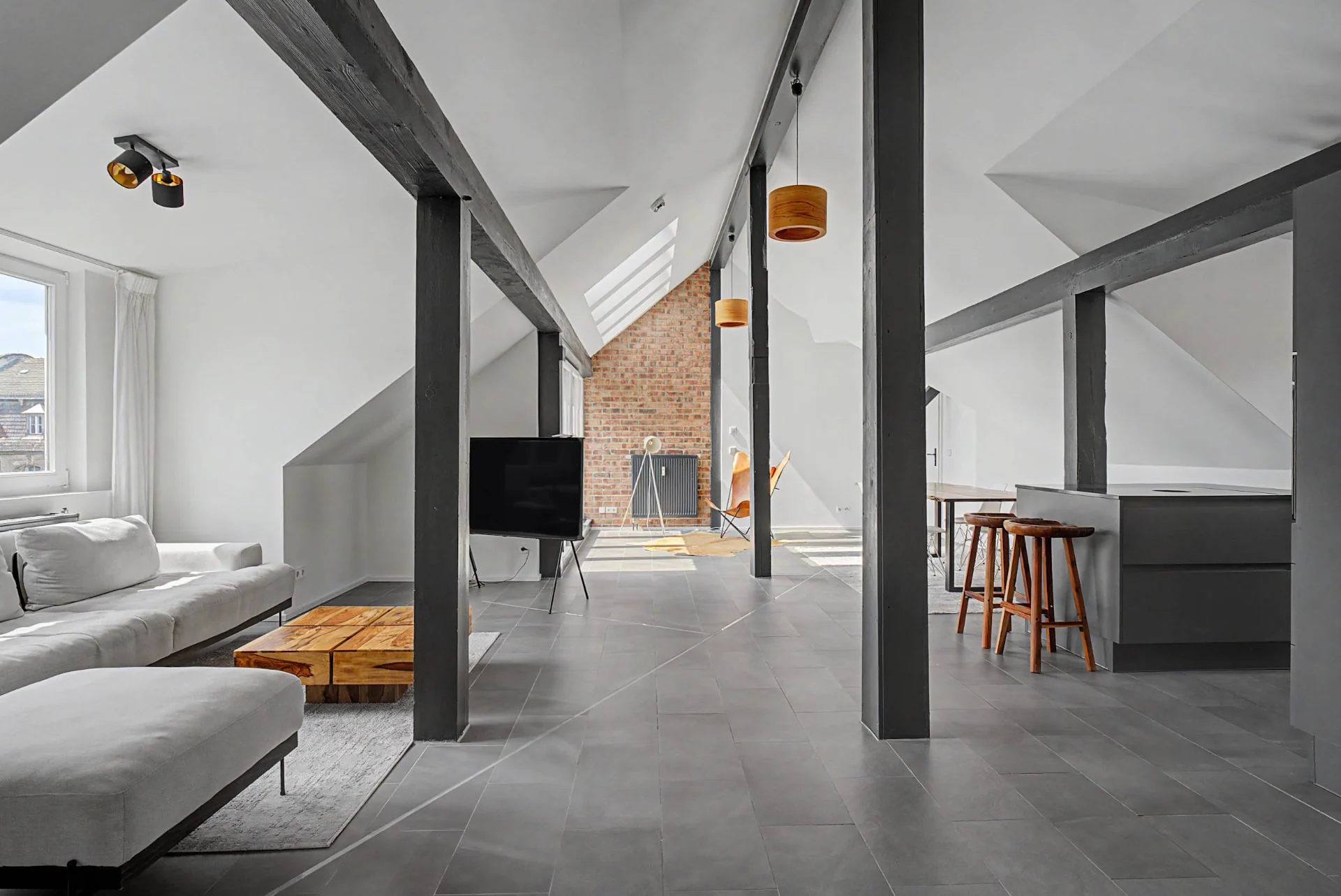 Offene Wohnfläche mit Sofa, Backsteinwand und schrägen Decken im umgebauten Loft in Berlin-Kreuzberg — Immobilienfotografie Berlin